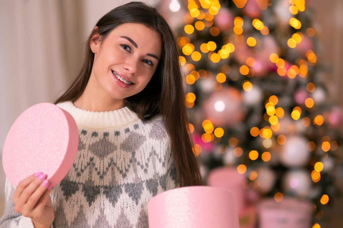 Woman holding pink gift boxes smiling near decorated Christmas tree indoors.