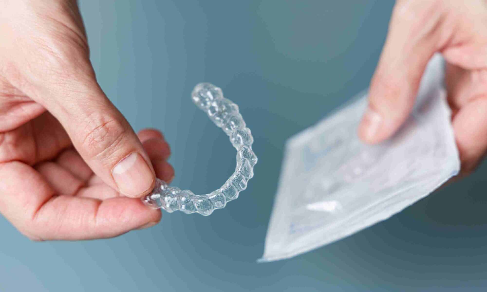 Hands holding a clear dental aligner and its packaging, illustrating clear aligner treatment and potential microplastic exposure